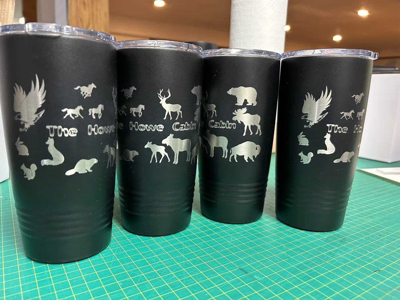 Four black tumblers engraved with wildlife scenes for a family cabin